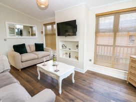 A living room with sofas a coffee table a wall-mounted television and windows with blinds at Finnbars Lodge in Richmond