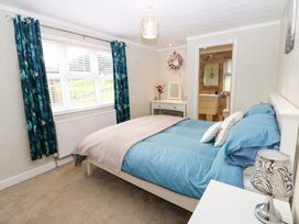 A bedroom with a bed blue bedding and beige blanket a white nightstand with lamp a window with blue curtains and a door leading to a bathroom at Finnbars Lodge Richmond