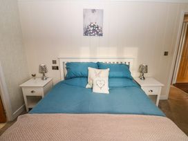 A bedroom with a blue bedspread two white bedside tables with lamps and a painting above the bed at Finnbars Lodge in Richmond