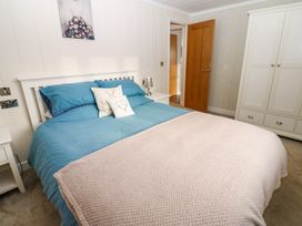 A bedroom with a double bed with blue bedding and beige blanket bedside tables a lamp a wardrobe and an open wooden door at Finnbars Lodge Richmond