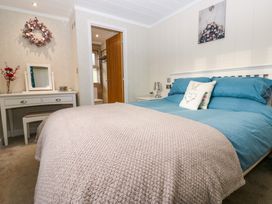 A bedroom with a bed covered in blue and beige bedding a dressing table with a mirror and flowers and an open door leading to a bathroom at Finnbars Lodge in Richmond