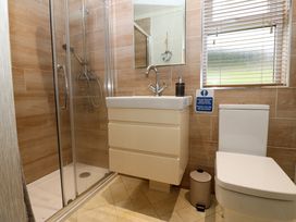 A bathroom with a shower enclosure a sink with a cabinet a toilet a small trash bin and a window with blinds at Finnbars Lodge in Richmond