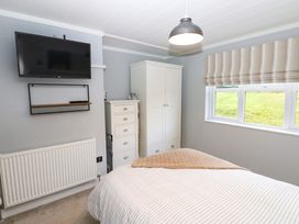 A bedroom with a mounted TV a white dresser a wardrobe a bed and a window at Finnbars Lodge Richmond