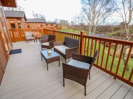 An outdoor deck with wicker chairs and a table overlooking a grassy area and other wooden cabins at Finnbars Lodge in Richmond
