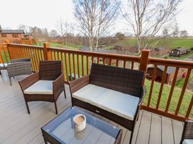 An outdoor wooden deck with wicker chairs and a glass coffee table overlooking green fields at Finnbars Lodge in Richmond