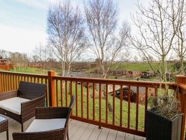 An outdoor balcony with rattan chairs and a planter overlooking a grassy area with trees and wooden cabins at Finnbars Lodge in Richmond