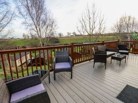 An outdoor deck with wicker chairs and tables overlooking a green field and trees at Finnbars Lodge in Richmond