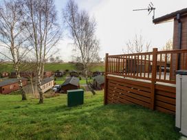 A grassy outdoor area with trees overlooking wooden cabins and a deck with railing at Finnbars Lodge in Richmond