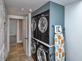 A laundry room with stacked washer and dryer and an ironing board at Snowdonia Manor in Dolgellau