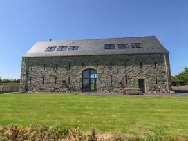 A stone barn with multiple windows and a large grass lawn at Tithe Barn in Capel Mawr near Malltraeth