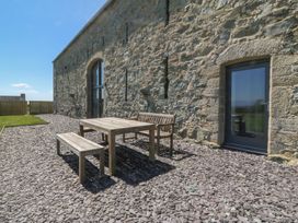 An outdoor patio with wooden table bench and chair on gravel beside a stone building at Tithe Barn in Capel Mawr near Malltraeth