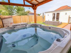 A covered hot tub in a fenced backyard with a wooden table and chairs and a patio seating area at Brimrod in Talacre