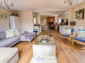 An open living room and kitchen with a grey sofa and two blue armchairs around a glass coffee table at Brimrod in Talacre