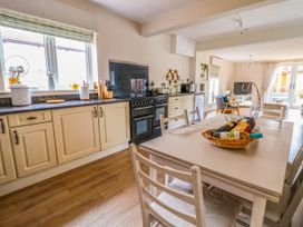 A kitchen and dining area with cream cabinets a black stove a table with chairs and a living room with a TV at Brimrod in Talacre