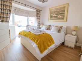 A bedroom with a bed, yellow throw, pillows, lamps, chest of drawers, window with curtains and a painting above the bed at Brimrod in Talacre