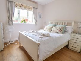 A bedroom with a white bed and bedside tables next to a window with floral curtains and a fan on the floor at Brimrod in Talacre