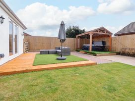 An outdoor patio area with a wooden deck artificial grass seating area and a covered hot tub at Brimrod in Talacre