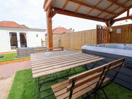 An outdoor covered seating area with a wooden table and benches next to a hot tub and a wicker sofa in the background at Brimrod Talacre