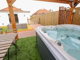 A covered outdoor area with a hot tub wooden table and chairs wicker sofa set and fenced yard at Brimrod in Talacre