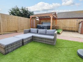 A backyard with outdoor sectional sofa on artificial grass and a hot tub under a wooden pergola at Brimrod in Talacre