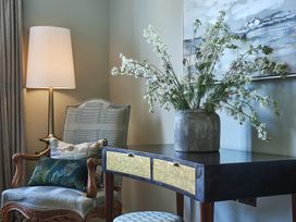 A living room with a chair, table, flowers and a lamp at Craig y Don in Glyngarth near Llandegfan