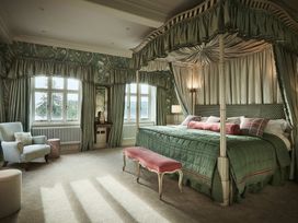 A bedroom with a four-poster bed, armchair, and windows at Craig y Don in Glyngarth near Llandegfan