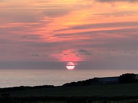 A sunset over the ocean with a silhouette of land at Badgers Sett Stibb near Kilkhampton