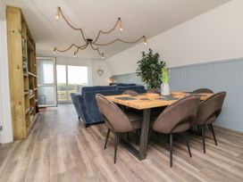 A dining area with a wooden table and chairs next to a living room with sofas and a bookshelf at La Bella Vista in Kilkhampton