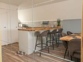 A kitchen with a wooden countertop and three bar stools next to a dining table with chairs and pet bowls on the floor at La Bella Vista in Kilkhampton