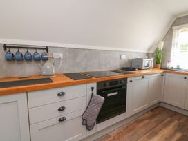 A kitchen with wooden countertop white cabinets a black oven a gray kettle blue mugs a microwave and a window with blinds at La Bella Vista in Kilkhampton