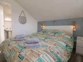 A bedroom with a double bed with patterned bedding gray towels on the bed a round mirror on the wall and an open door showing a sink at La Bella Vista in Kilkhampton