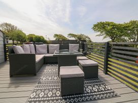 An outdoor deck with a sectional sofa, cushioned stools, a glass table, and a patterned rug at La Bella Vista in Kilkhampton