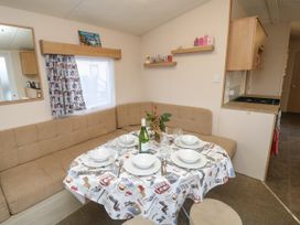 A dining area with a table set with plates glasses cutlery and a bottle next to a beige corner sofa at Dunlin Walk 13 in Hayling Island