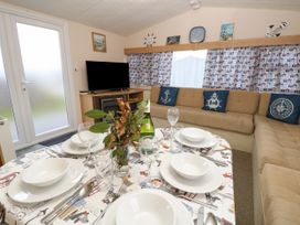 A dining table set with white dishes and glasses in a living room with a beige sectional sofa and a television at Dunlin Walk 13 Hayling Island