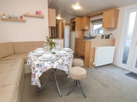A dining area with a round table set with bowls plates and glasses next to a beige corner sofa and a kitchen with wooden cabinets at Dunlin Walk 13 in Hayling Island
