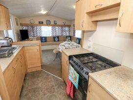 A kitchen with gas stove and wooden cabinets opening to a living room with sofa and dining table at Dunlin Walk 13 in Hayling Island