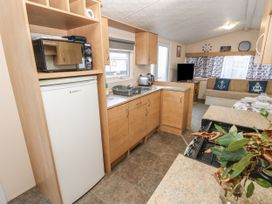 A kitchen area with wooden cabinets a refrigerator a microwave a sink and a living space with sofa and television at Dunlin Walk 13 Hayling Island