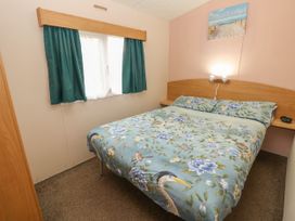 A bedroom with a double bed with floral and bird patterned bedding a window with curtains and a wall-mounted light at Dunlin Walk 13 in Hayling Island