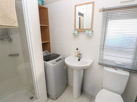 A bathroom with a shower, washing machine, sink, toilet, and window blinds at Dunlin Walk 13 in Hayling Island