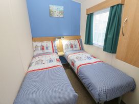 A bedroom with two single beds with patterned bedding a small shelf with lights and a window with curtains at Dunlin Walk 13 in Hayling Island