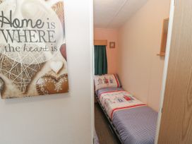 A small bedroom with a single bed and patterned bedding with a green curtain and a wall sign saying home is where the heart is at Dunlin Walk 13 Hayling Island