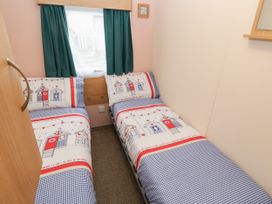 A small bedroom with two single beds with seaside themed bedding and green curtains at Dunlin Walk 13 in Hayling Island
