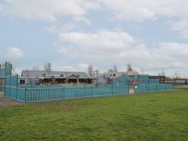 A fenced outdoor basketball court and playground area with buildings and grassy field at Dunlin Walk 13 in Hayling Island