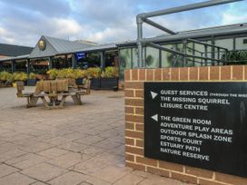 Outdoor seating area with wooden picnic tables and a building with plants and windows at Dunlin Walk 13 Hayling Island