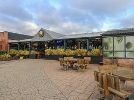 An outdoor seating area with wooden tables and chairs in front of a building with plants and large windows at Dunlin Walk 13 in Hayling Island