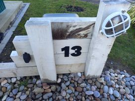 A wooden fence post with the number 13 and a light fixture surrounded by stones and grass at Dunlin Walk 13 Hayling Island