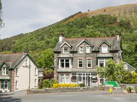 A large stone house with multiple windows and chimneys next to a road with directional signs in front of a forested hill