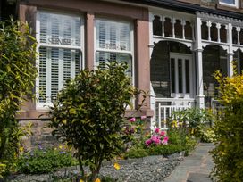 Front garden with flowering plants and shrubs in front of a house with stone walls and white window shutters at Sunnycroft in Keswick