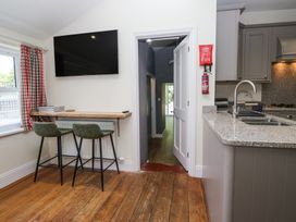 A kitchen area with two bar stools at a counter under a wall-mounted TV and an open door showing a hallway at Sunnycroft in Keswick