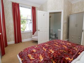 A bedroom with a bed covered by a patterned blanket a striped chair near a window with red curtains and a wardrobe next to an open door leading to a bathroom at Sunnycroft in Keswick